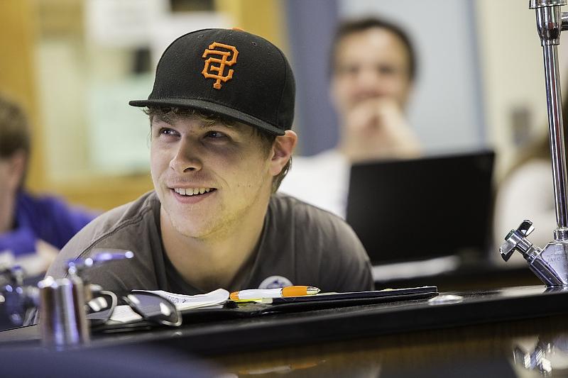 Student in baseball cap smiles while seated at science lab table