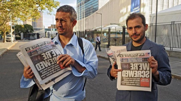 Yes Men on city street holding newspapers